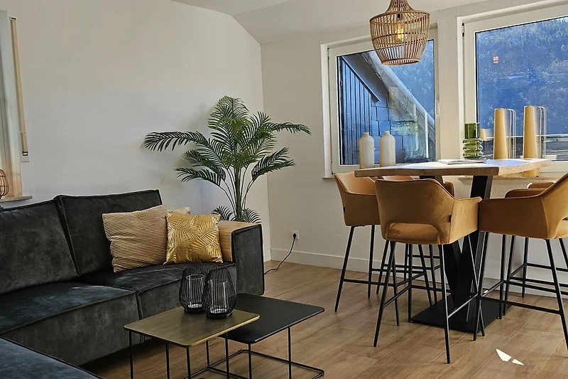 Offener Wohnbereich mit Holzdetails, Sofa, Esstisch und Pflanzen.