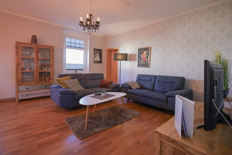 Wohnzimmer mit Sofa, Fernseher, Holzdecke, Leuchte und Pflanzen.