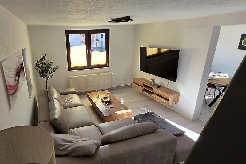 Wohnbereich mit Sofa, Couchtisch, TV und großem Fenster.