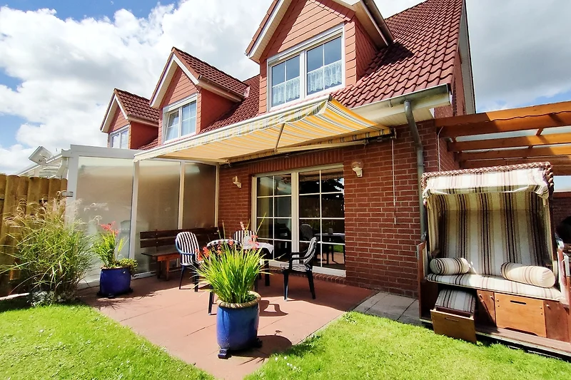 Überdachte Terrasse mit Gartenmöbeln, Tisch und Pflanzen im Grünen.