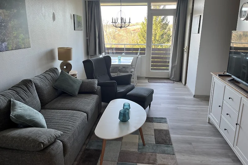 Großzügiger Wohnbereich mit Sofa, Sessel, TV und Esstisch aus Holz.