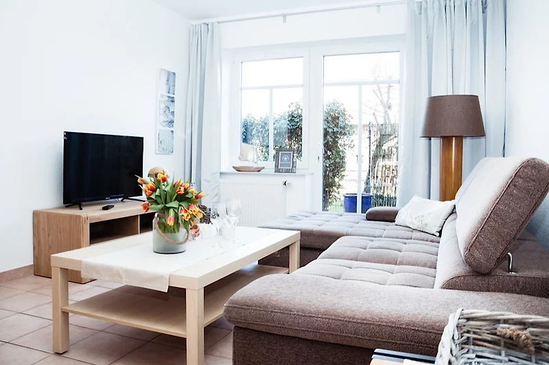 Großzügiger Wohnbereich mit Sofa, TV und viel Tageslicht.
