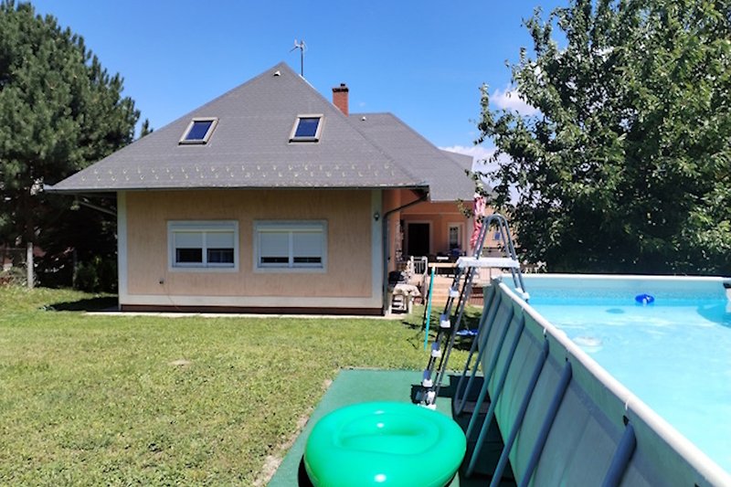 Großer Garten mit Pool, umgeben von Bäumen und grüner Wiese.