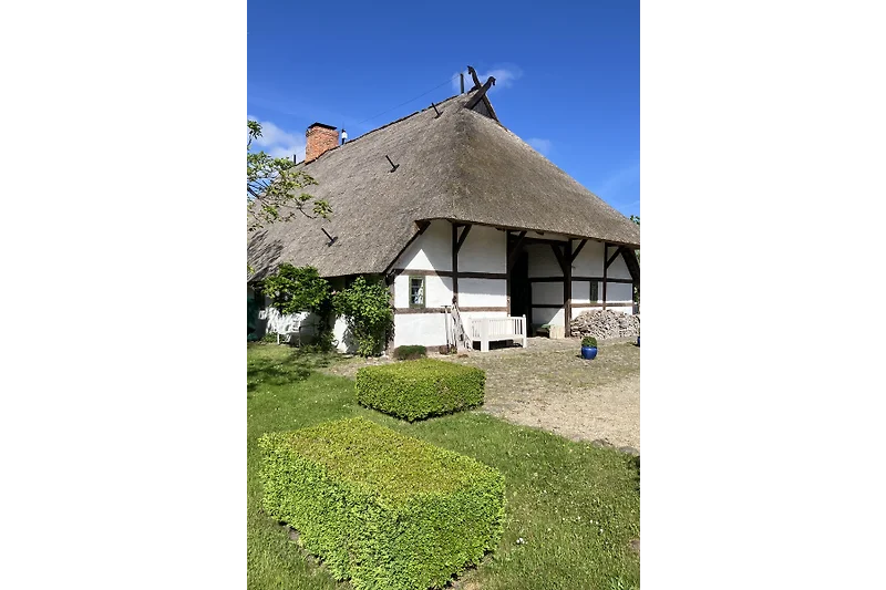 Reetgedecktes Haus mit gepflegtem Garten, Einfahrt und Dorfblick.