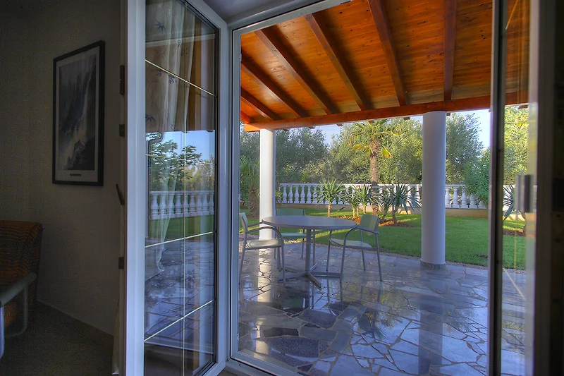 Überdachte Veranda mit Holzdecke, Glastür und bequemen Sitzmöbeln.