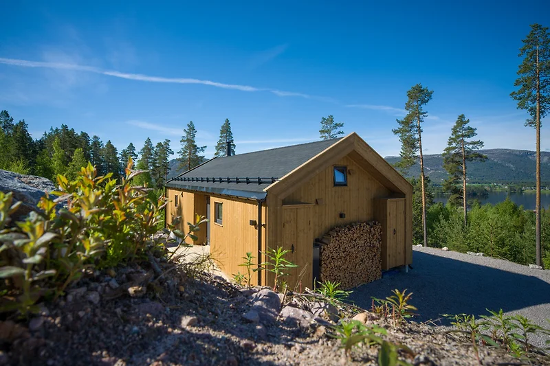 Blockhaus mit Satteldach, umgeben von Tannen und ländlichen Nebengebäuden.