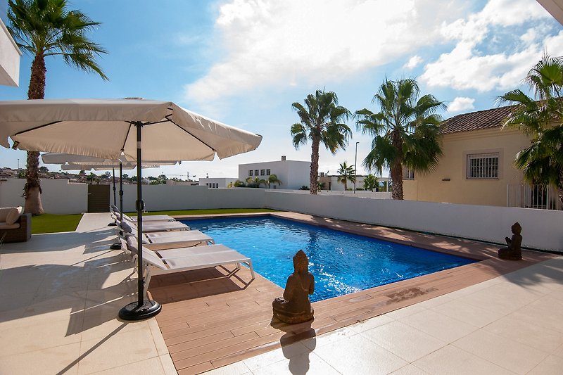 Schwimmbad mit Sonnenliegen und Palmen in einem Resort.