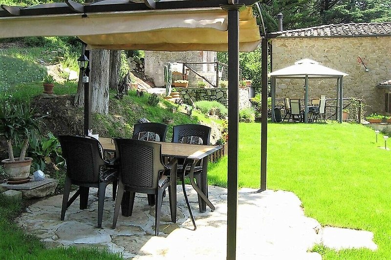 Una casa di campagna con un patio ombreggiato, tavolo e sedie all'aperto.