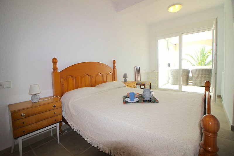 Schlafzimmer mit Holzmöbeln, Bett, Fenster und Gitarre.