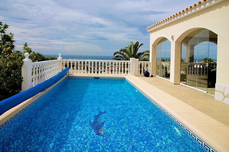 Luxuriöses Ferienhaus mit Pool, Palmen und blauem Himmel.