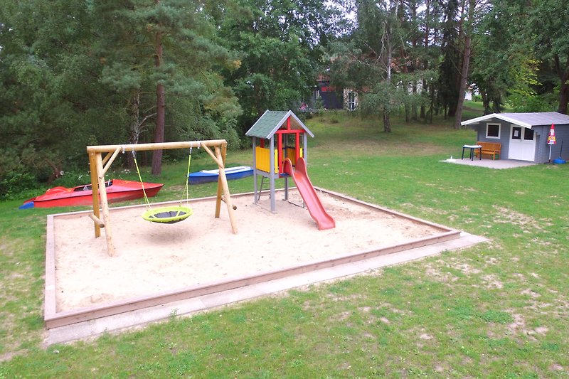Spielplatz mit Schaukel, Rutsche und Grasfläche.