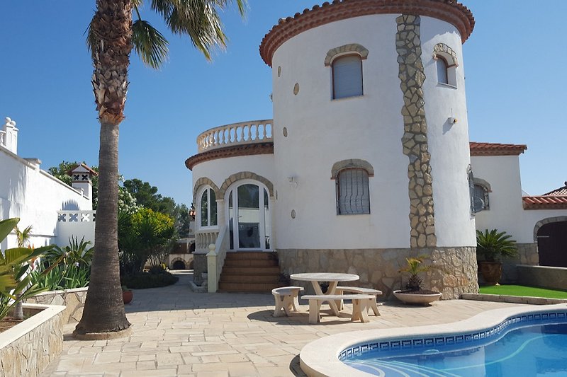 Schöne Villa mit Pool, Palmen und blauem Himmel.