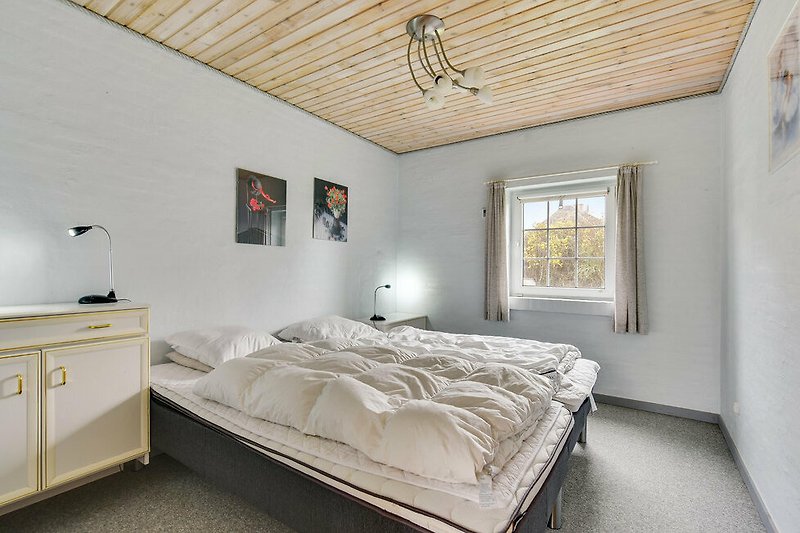 Schlafzimmer mit bequemem Bett, Fenster und Holzmöbeln.