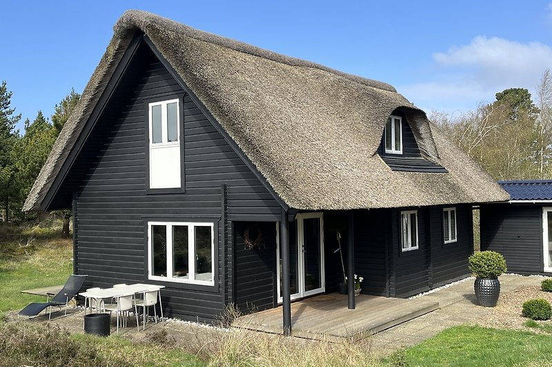 Holzhaus mit thatched Dach, Fenster und grünem Garten.