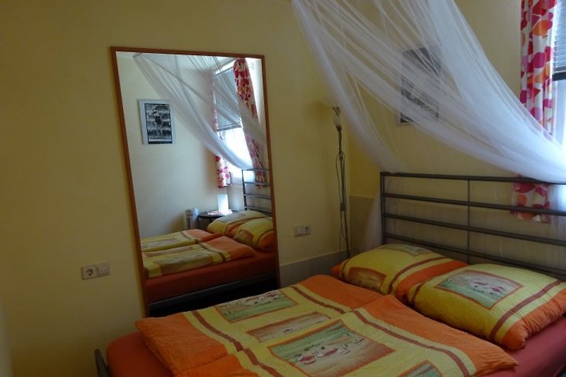 Sypialnia z moskitierą na oknie i nad łóżkiem.