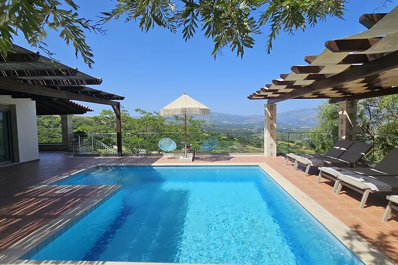 Villa mit Pool, Palmen und schattenspendender Pergola.