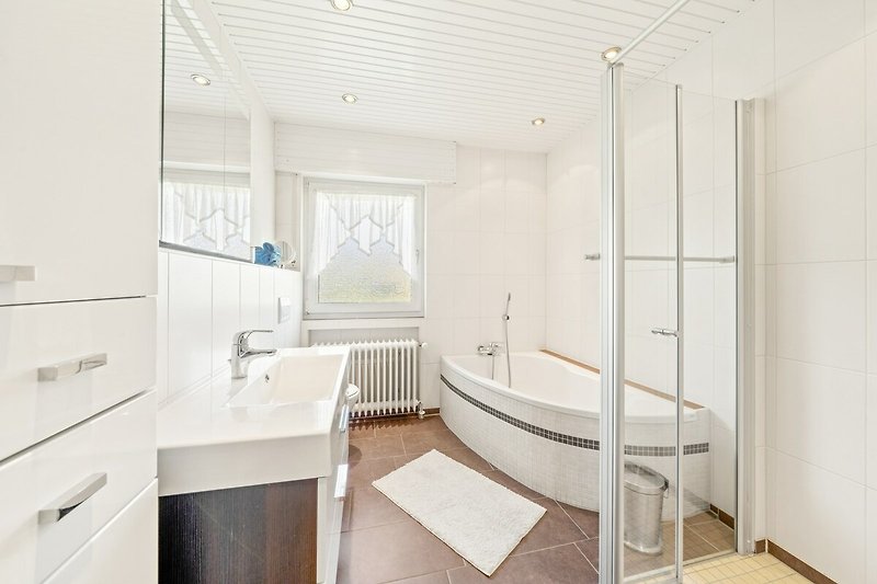 Modernes Badezimmer mit Badewanne, Fenster und Deckenbeleuchtung.