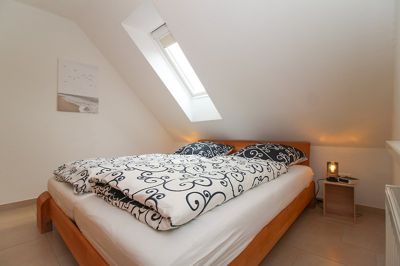 Schlafzimmer mit gemütlichem Bett, Nachttisch, Lampe und Fenster.