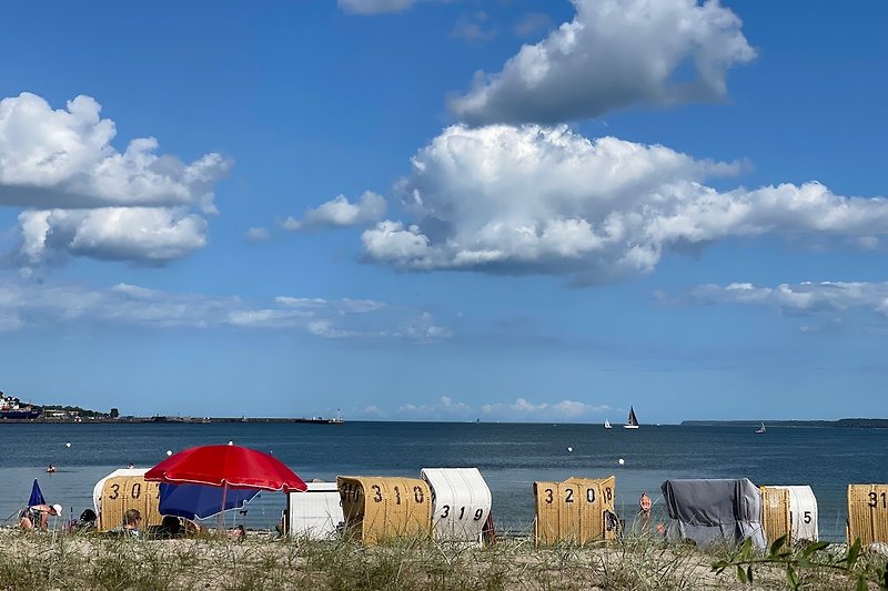 Schöner Strand in Eckernförde mit blauem Wasser, Sonnenschirmen und Menschen.