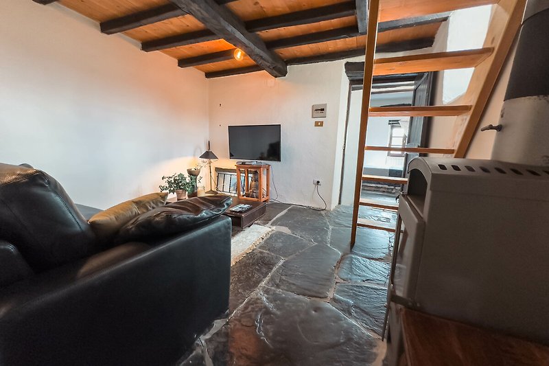 Wohnzimmer mit Holzbalken, gemütlicher Couch und TV