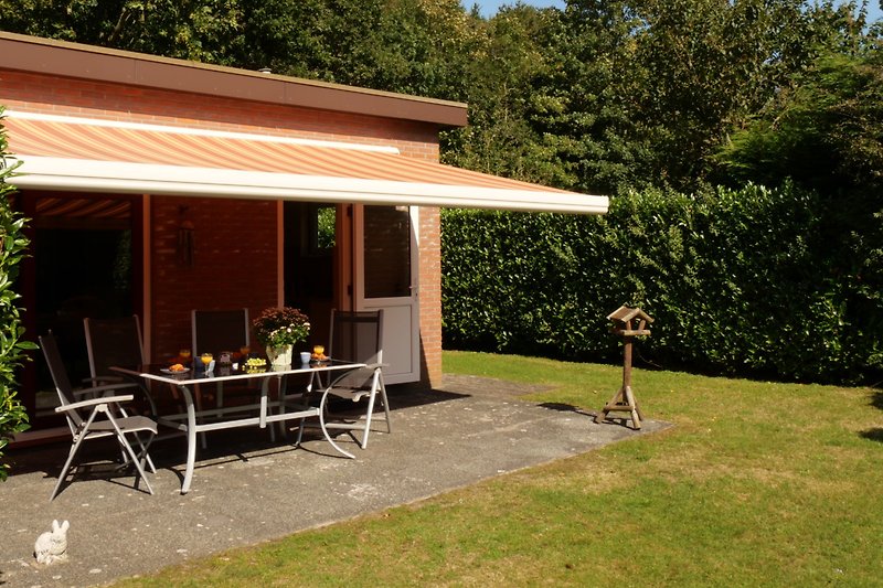 Garten mit Pergola, Tisch und Stühlen, umgeben von Bäumen.