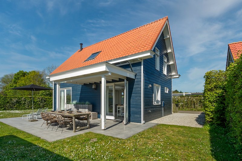 Ländliches Haus mit grünem Garten, blauem Himmel und Wolken.