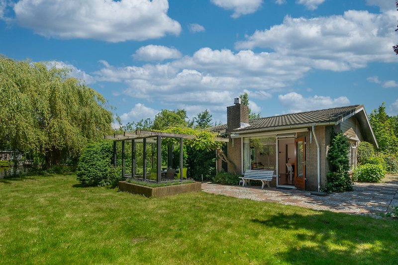 Charmantes Landhaus mit Garten, Bäumen und blühenden Sträuchern.