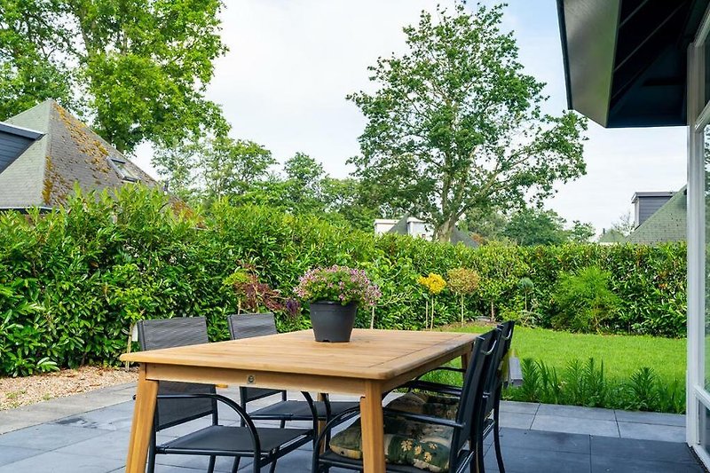 Schöne Terrasse mit Holzmöbeln, Blumen und grünem Garten.