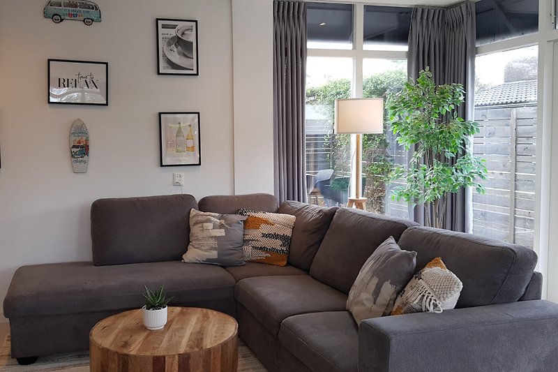 Wohnzimmer mit brauner Couch, Pflanze, Holzmöbeln und Fensterblick.