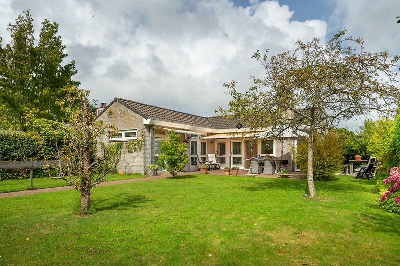 Charmantes Landhaus mit Garten, Bäumen und blühenden Sträuchern.