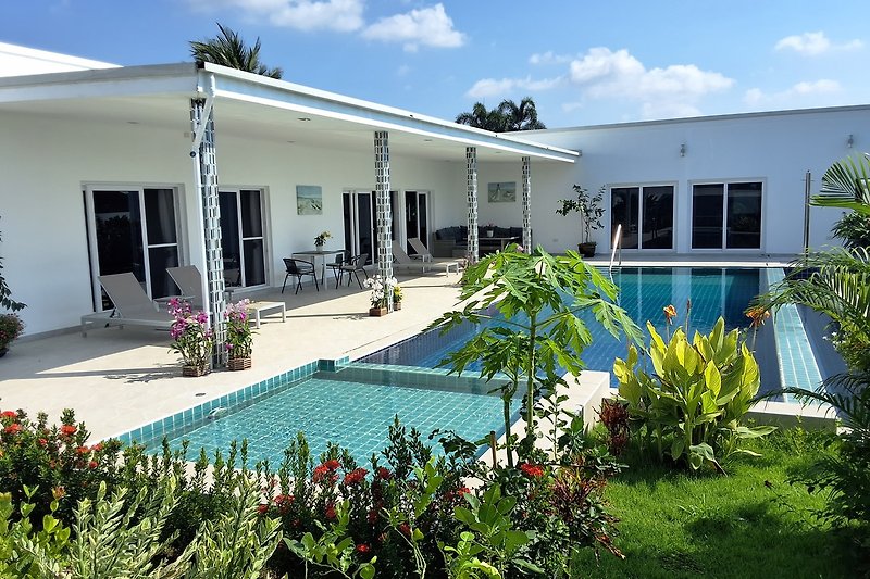 Luxuriöse Villa mit Pool, tropischer Garten und stilvollen Outdoor-Möbeln.