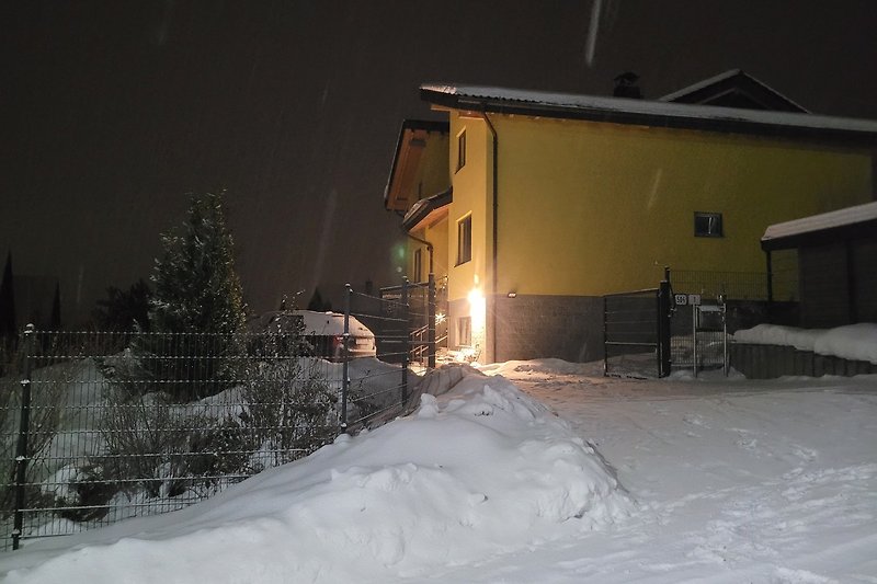 Winterliches Haus mit verschneiter Landschaft und beleuchtetem Fenster.