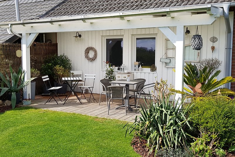 Ferienhaus mit Gartenmöbeln, Sonnenschirm und Blumen - perfekt für Entspannung.