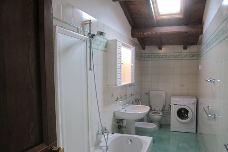 De badkamer met ligbad en douche, wastafel, bidet en toilet. De wasmachine.