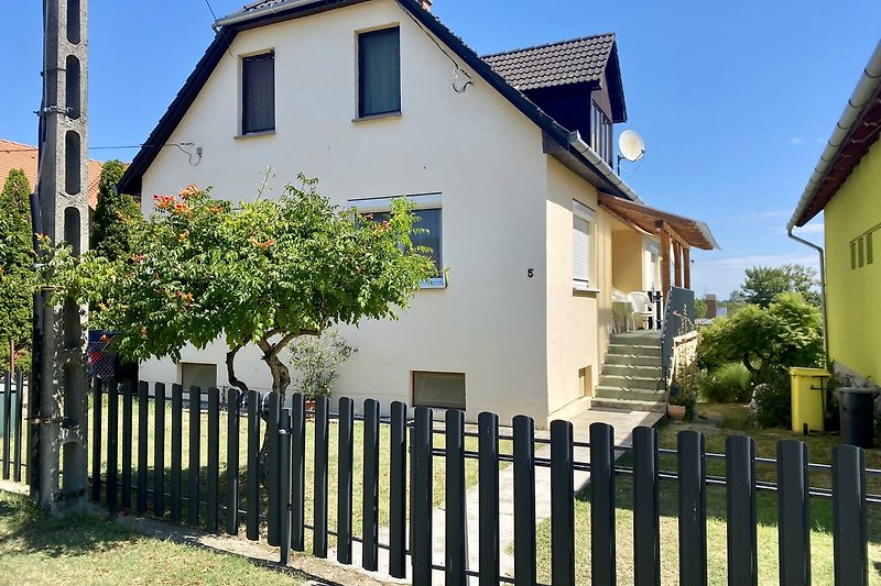 Gemütliches Landhaus mit Garten, Holzzaun und blühenden Sträuchern.