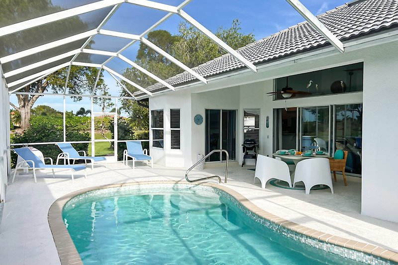 Luxuriöses Ferienhaus mit Pool, Sonnenliegen und blauem Himmel.