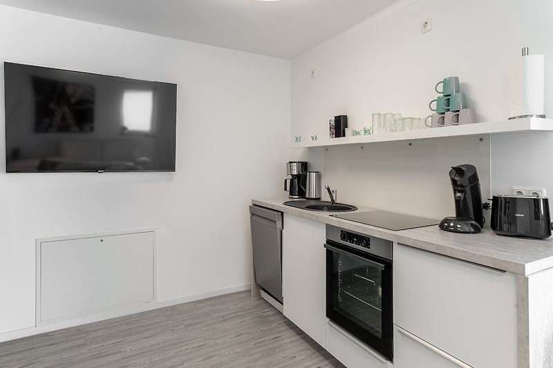 Moderne Küche mit weißer Einbauküche, grauer Arbeitsplatte und großer Streaming-TV.