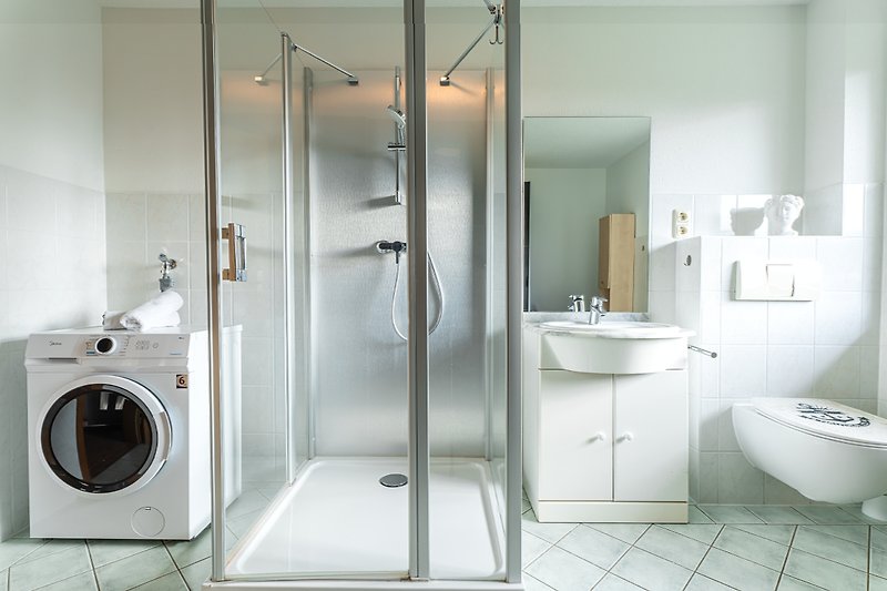 Modernes Badezimmer mit Waschmaschine, Spiegel, Dusche und Waschbecken.