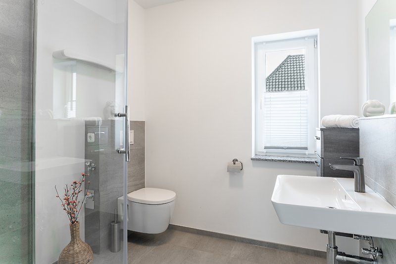 Modernes Badezimmer mit Dusche, WC und Fenster.