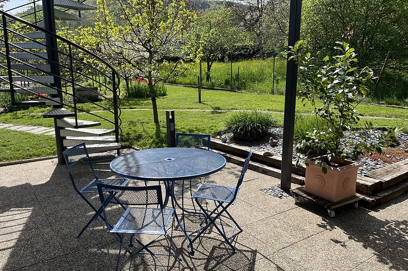 Garten mit Tisch, Stühlen, Pflanzen und Bäumen. Gemütliche Outdoor-Möbel.