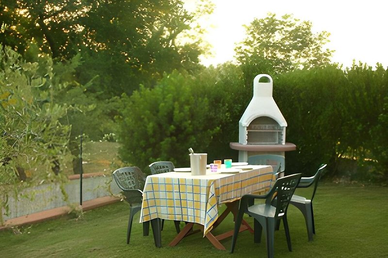 Privater Garten mit Grill, Tisch, Stühlen und einem Olivenbaum. Gemütlicher Ort zum Entspannen im Freien.