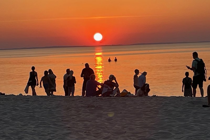 Strandurlaub bei Sonnenuntergang mit Menschen am Meer.