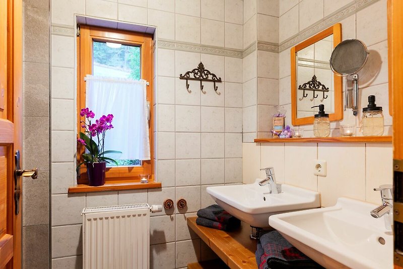 Spiegel, Waschbecken und lila Blume in einem Badezimmer.