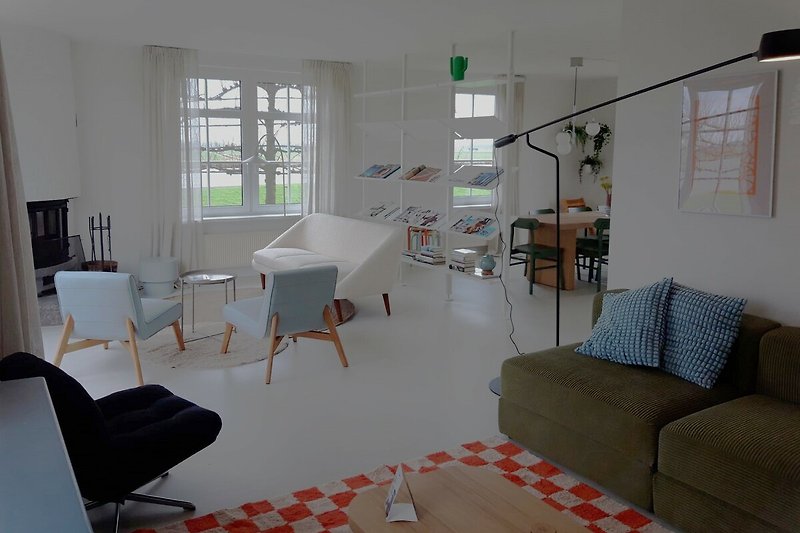 Modernes Wohnzimmer mit weißem Mobiliar, Holzboden, großen Fenstern und gemütlicher Couch.