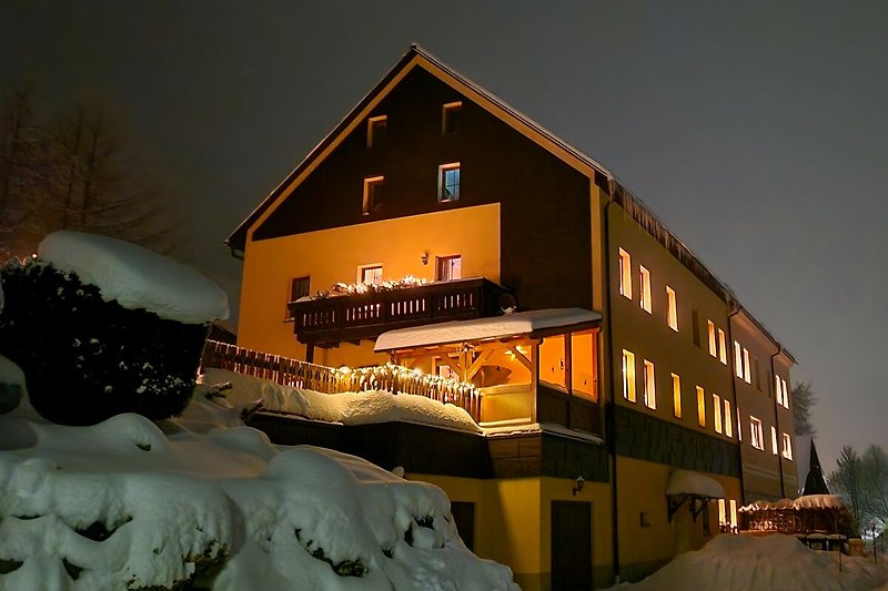 Winterlandschaft mit verschneitem Haus, beleuchteten Fenstern  Perfekt für einen winterlichen Urlaub.
