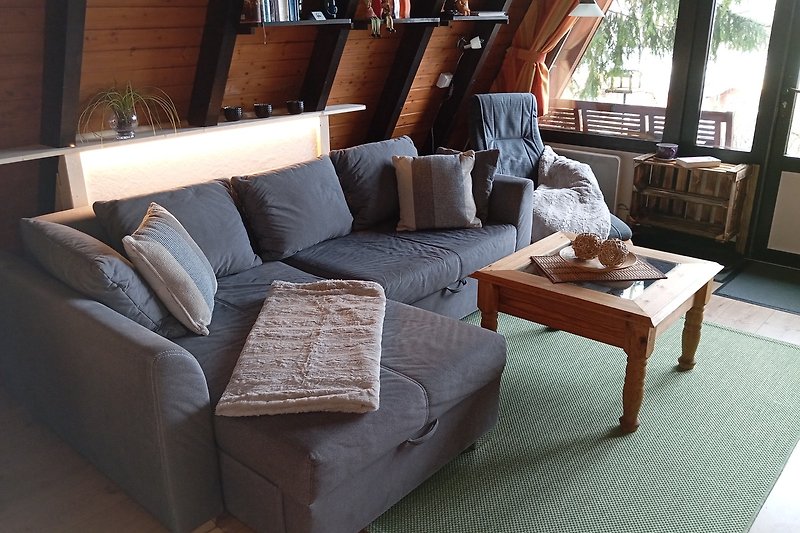 Gemütliches Wohnzimmer mit einer ausziehbaren Couch, Holzmöbeln und bequemen Kissen.
