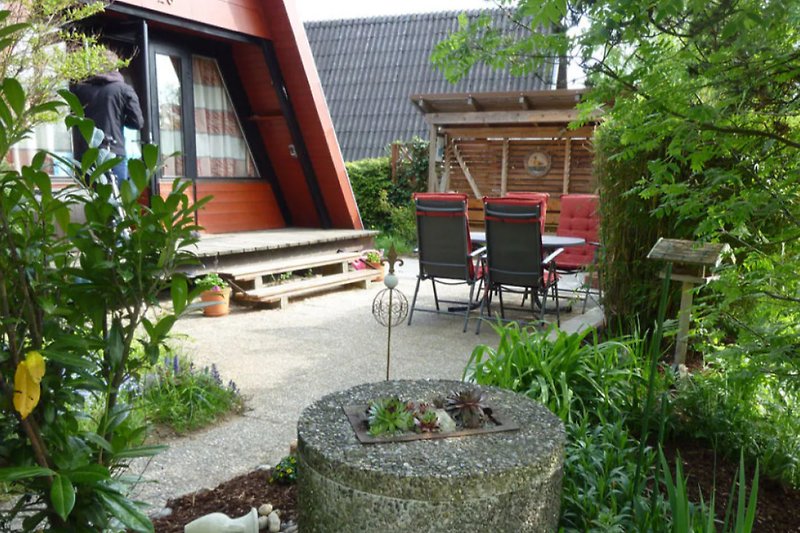 Gemütlicher Garten mit Holzterrasse, Gartenmöbeln und blühenden Sträuchern.