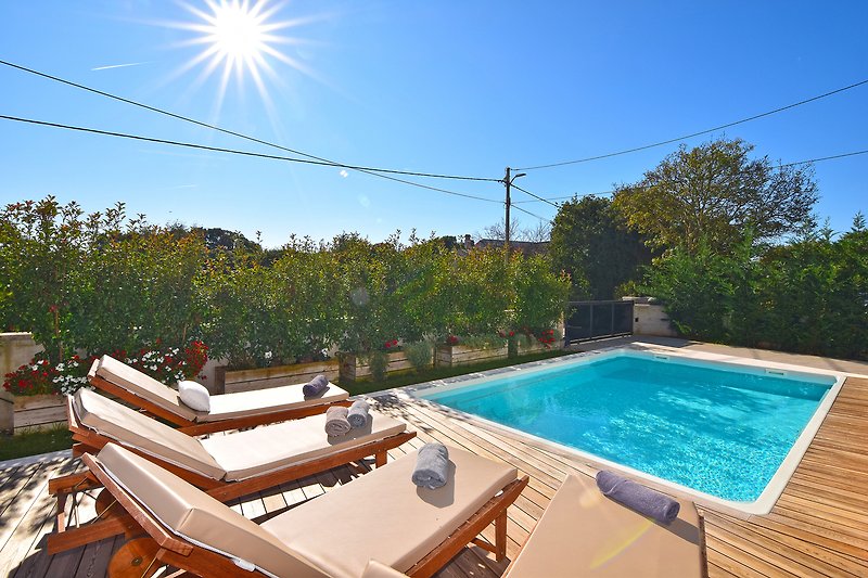 Villa mit Pool, Sonnenliegen und üppiger Gartenlandschaft.