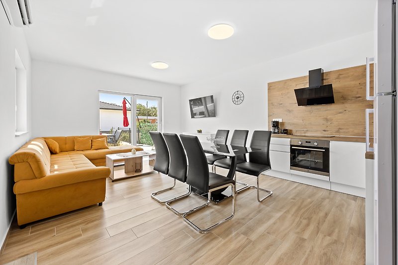 Helles Wohnzimmer mit Couch, Tisch, Pflanzen und großem Fenster.