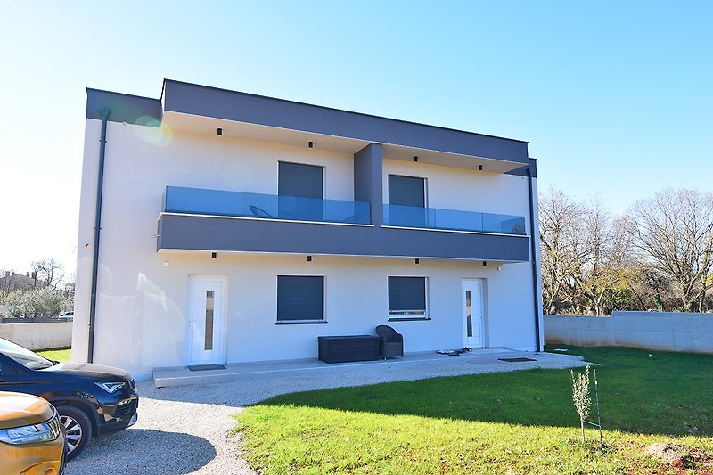Modernes Haus mit blauem Himmel, grünem Garten und Auto.